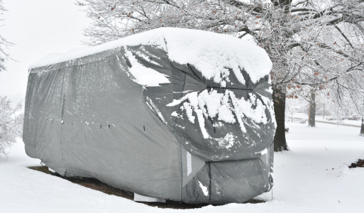 RV covered with a protective winter cover in a snowy landscape